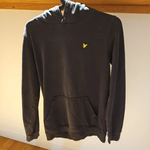 Svart Hoodie Från Lyle & Scott | Storlek 12/13 år/152 - Snygg och stilren Lyle & Scott Junior huvtröja i svart. Tröjan har en klassisk design med en liten logotyp på bröstet och en praktisk ficka i fram. Perfekt för både vardag och fritid. Kan diskutera om ett annat pris. Skriv om ni har minsta fundering