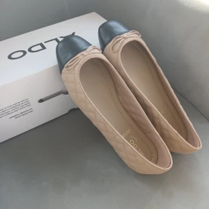 ballerinaskor i läder. Strl 41, Aldo - Snygga ballerinaskor från Aldo i beige med svart tå. Skorna har en quiltad design och en söt rosett framtill. Perfekta för en stilren look.