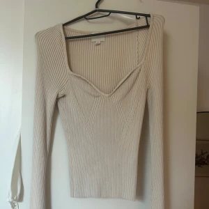 Beige ribbad topp - Säljer en stilren beige ribbad topp med lång ärm och v-ringad design. Perfekt för en chic och enkel look. Passar bra till både jeans och kjol. Hör av dig vid intresse!