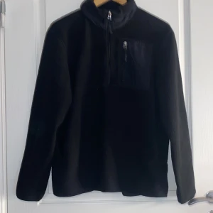 Svart fleecejacka från H&M - Säljer en svart fleecejacka från H&M i storlek M. Jackan har en halv dragkedja framtill och en praktisk bröstficka med dragkedja. Perfekt för kyliga dagar med sin mjuka och varma fleece.