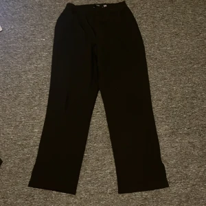 Svarta byxor med slits - Snygga svarta byxor med en diskret slits vid benslutet. De har en rak passform och är perfekta för en stilren look. Byxorna är tillverkade i ett mjukt material som ger en bekväm känsla hela dagen. Med fickor vid sidorna 