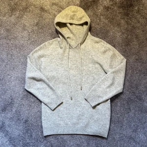 Grå merinoulls hoodie - Säljer en stilren grå merinoulls hoodie med långa ärmar och justerbar huva. Perfekt för kyliga dagar och ger en avslappnad look. Storlek S. 