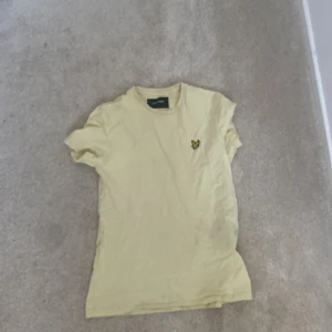 Gul t-shirt från Lyle & Scott - Säljer en gul t-shirt från Lyle & Scott med deras ikoniska logga på bröstet. T-shirten är kortärmad och har en klassisk rund halsringning. Perfekt för en avslappnad stil.