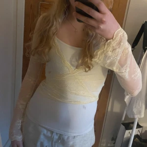 Krämfärgad spetsblus från Venderby's - Säljer en elegant krämfärgad spetsblus från Venderby's. Blusen har långa ärmar och ett omlottmönster med knytband i midjan. Perfekt för en stilren look med en touch av romantik. Ursprungligt pris över 60€.