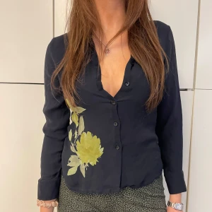 Marinblå blus med blomdetalj  - Supersöt marinblå blus med blomdetalj och knäppning! Så fin och i så skönt material! Tjejen på bilden är 175 cm lång och blusen är i storlek S! 