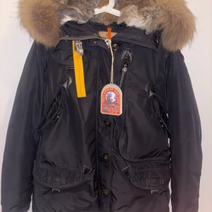 Svart parkajacka från Parajumpers - Säljer en svart parkajacka från Parajumpers i nyskick. Jackan har en stor huva med pälsdetaljer och är perfekt för vintern. Den har både dragkedja och knappar framtill, samt flera praktiska fickor. Insidan är quiltad för extra värme. Passar perfekt för kalla dagar! Köptes i Januari 2024 för 11500kr