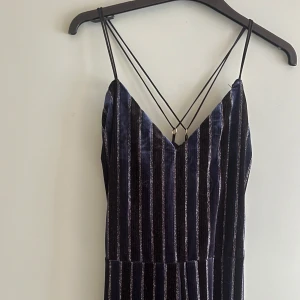 Blå- & svartglittrig jumpsuit i  - Svart jumpsuit med blåa och silvriga ränder. Vida ben i plyschmaterial.   Korsade band i ryggen. Inga tecken på användning. 