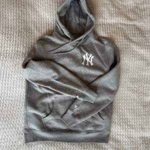 Säljer en grå hoodie från New York Yankees i storlek XL. Den har en stor logga på framsidan och flera tryck på baksidan med Yankees-tema. Perfekt för höst och vinter, och den är superbekväm med en känguruficka och justerbar huva. Nytt skick, aldrig använd. Går liten i storlek, passar mer som M/L.