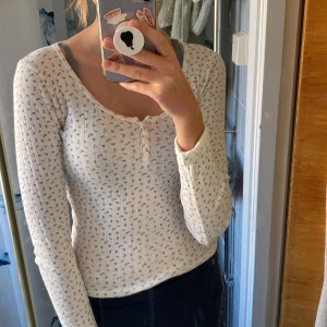 Vit blommig topp från Brandy Melville - Säljer en superfin vit topp från Brandy Melville med små blommor i lila och grönt. Den är långärmad och har en söt knappdetalj på framsidan💗 har inte exakt koll på storlek men till längd är den perfekt för 160