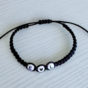 Svart armband med bokstavspärlor(Nytt armband görs vid varje köp!) - Säljer ett snyggt svart armband med justerbar knytning. Armbandet har vita bokstavspärlor med bokstäverna 'E', 'L' och ett hjärta emellan. Perfekt för att ge bort som en personlig present eller bära själv för en stilren look.(valfri text )