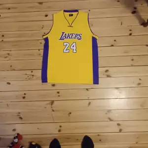 Säljer ett gult Lakers basketlinne med nummer 24 på både fram- och baksidan. Linnet har lila detaljer på sidorna och ärmlös design. Perfekt för basketfans eller som en cool streetwear-stil.