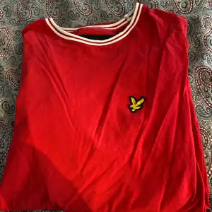 Säljer en snygg röd t-shirt från Lyle & Scott med deras ikoniska logga på bröstet. T-shirten har en vit randig krage som ger en sportig look. Perfekt för vardagsbruk eller en avslappnad dag ute. Passar bra till jeans eller shorts!