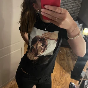 Svart t-shirt med tryck - Säljer en svart t-shirt med ett stort tryck av en kvinna på framsidan.