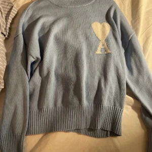 Ljusblå stickad tröja från Ami - Säljer en superfin ljusblå stickad tröja från Ami. Tröjan har en normal passform, perfekt för alla årstider. Den är i helt nytt skick och har ribbade muddar vid ärmslut och nederkant. Passar perfekt för en stilren och mysig look! Nypris runt 4500. Säljer då den var för liten