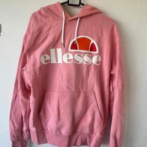 Säljer en superfin rosa hoodie från Ellesse i bra skick. Den har en stor logga på framsidan och en mysig huva med vita snören. Perfekt för chilliga dagar eller när du vill ha en sportig look. Stor ficka fram för att värma händerna eller förvara småsaker.