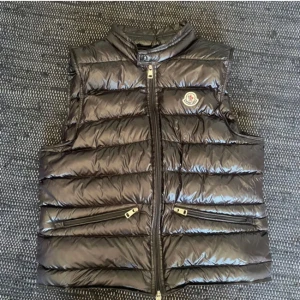 Svart dunväst från Moncler - Säljer en snygg svart dunväst från Moncler i mycket bra skick. Västen har en glansig finish och dragkedja framtill. Perfekt för höst och vinter, och den har praktiska fickor med dragkedjor. En stilren och varm väst för kyligare dagar. Den är i nyskick 10/10 och den är äkta såklart! Byten är också intressant 