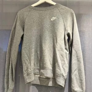 Grå sweatshirt från Nike - Säljer en grå sweatshirt från Nike i mycket bra skick. Den har en klassisk design med rund hals och långa ärmar. Perfekt för både vardag och träning. Nike-loggan är broderad i vitt på bröstet. Superbekväm och stilren! Använd gärna köp nu 💕