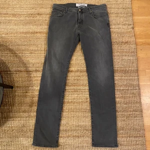 Grå jeansbyxor från Jacob Cohen - Säljer ett par snygga grå jeansbyxor från Jacob Cohen. De har en slim passform och är i mycket bra skick. Perfekta för både vardag och fest! Byxorna har en klassisk femficksdesign och en knappgylf. De är tillverkade i ett mjukt och bekvämt material.