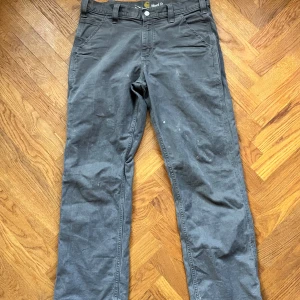  Carhartt byxor - Säljer ett par grå Carhartt-byxor i relaxed fit Riktigt feta o passar t olika stilar. Byxorna har flera fickor på sidorna. Perfekta för vardagsbruk eller arbete. Några små fläckar finns, syns på bilderna, men de är i bra skick överlag och inga hål.