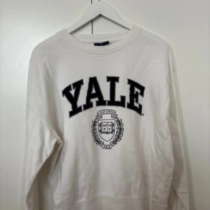 Vit Yale sweatshirt - Säljer en vit sweatshirt med Yale-logga i svart. Tröjan har långa ärmar och är i bra skick men har en liten fläck på ena ärmen.