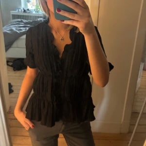 Svart blus med volangdetaljer - Jättefin svart blus med volangdetaljer och korta ärmar. Superfint skick❤️ Storlek xs men jag brukar vanligtvis vara i storlek s så den är stor i storleken!