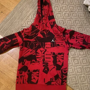 Röd och svart hoodie från Jordan - Säljer en cool röd och svart hoodie från Jordan med ett unikt mönster och den ikoniska loggan på bröstet. Perfekt för streetwear-stilen med en bekväm passform och huva.