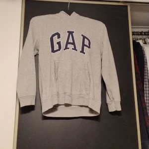 Grå hoodie från GAP Kids - Säljer en grå hoodie från GAP Kids med stor logga på . Tröjan har en klassisk känguruficka och långa ärmar. Perfekt för en avslappnad stil. Pris kan diskuteras.