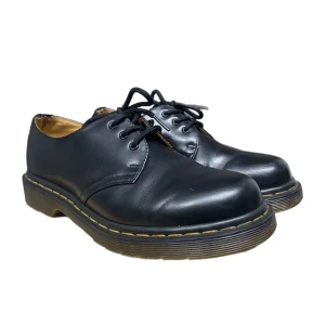 Svarta Dr. Martens skor - Klassiska svarta Dr. Martens skor i skinn med snörning och den ikoniska gula sömmen runt sulan. Perfekta för en stilren och tidlös look.