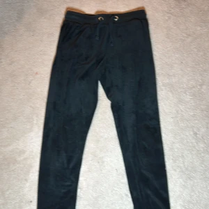 Svarta mjukisbyxor från Juicy Couture - Snygga svarta mjukisbyxor från Juicy Couture med glittrig logga längs benet. Byxorna har en bekväm passform med snörning i midjan och en bakficka. Perfekta för en avslappnad stil.Juicy couture märket kommer vid sidan av höger ben! De är även äkta…