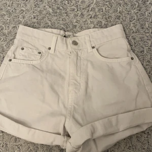 Vita jeansshorts från Gina tricot - Snygga vita jeansshorts från Gina tricot med hög midja och klassisk femficksdesign. De har en knappgylf och uppvikta benslut för en avslappnad look. Perfekta för sommardagar!