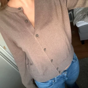 Beige/brun kofta med knappar - Säljer en stilren beige/brun kofta med knappar framtill. Koftan har långa ärmar och en rund halsringning, perfekt för en avslappnad look. Passar bra till jeans eller kjol. Storlek l men är mer en m.