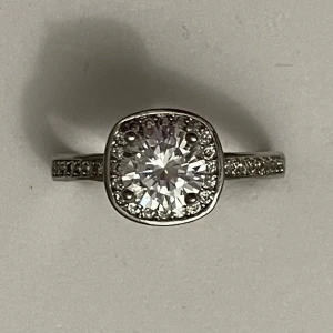 Silverring med glittrig sten - Elegant silverring med en stor, glittrig sten i mitten omgiven av mindre stenar. Bandet är dekorerat med små gnistrande stenar som ger extra glans. Perfekt för speciella tillfällen eller som en vacker accessoar till vardags.