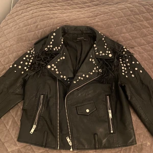 Svart skinnjacka med nitar från Zara Basic - Snygg svart skinnjacka från Zara Basic med coola nitar och fransdetaljer. Jackan har dragkedja och flera fickor. Ifall man inte vill ha fransdetaljerna så ser det enkelt ut att klippa bort 💕 Storlek L men skulle säga att det snarare är en s/m. 