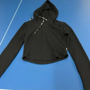 Svart ribbad hoodie från Stronger - Snygg svart ribbad hoodie med croppad passform och långa ärmar. 