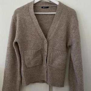 Populär kofta från Gina Tricot - Mysig beige kofta från New Look med v-ringning och knappar framtill. Den har två praktiska fickor och ribbade muddar vid ärmslut och nederkant. Perfekt för kyliga dagar!