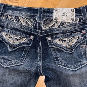 Blå jeans från Miss Me - Snygga blå jeans från Miss Me med unika detaljer på bakfickorna. Jeansen är skinny passform och är dekorerade med broderier och paljetter. Perfekta för att ge din outfit en extra touch.
