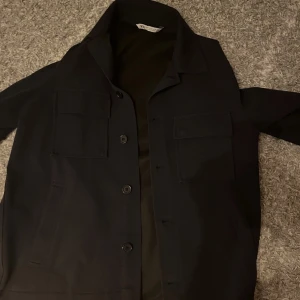  Overshirt från Zara - Snygg mörkblå overshirt från Zara med knappar framtill och två bröstfickor. Perfekt för en stilren look. Jackan har en klassisk krage och är långärmad.