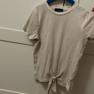Beige topp från XOXO Friends - Säljer en beige ribbad topp från XOXO Friends med korta ärmar och knytning framtill.