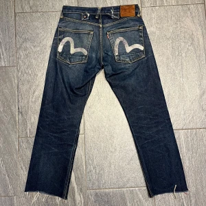 Mörkblå evisu jeans med unik bakficka - Snygga mörkblå jeans med en cool design på bakfickorna. Snygg wash. Längd 91cm midjemått 38cm fotvidd 21cm 