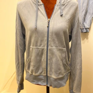 Ljusblå huvtröja med dragkedja från Cubus L - Mysig ljusblå huvtröja från Cubus med dragkedja och två fickor framtill. Tröjan har ett hjärtmönster i strass på bröstet och justerbar huva med snören. Perfekt för en avslappnad stil.