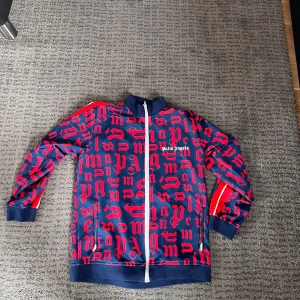 Blå och röd kofta från Palm Angels - Snygg rödblå kofta från Palm Angels  koftan har långa ärmar och en hög krage. Perfekt för en cool och avslappnad stil.