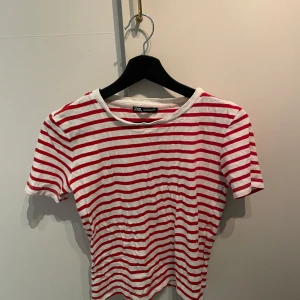 Randig t-shirt från Zara - Säljer en snygg randig t-shirt från Zara i rött och vitt. Den har korta ärmar och en rund halsringning. Perfekt för en avslappnad stil.