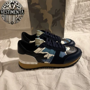 Valentino Rockrunner  - Snygga Valentino Rockrunner sneakers med ett coolt camouflage-mönster i blått, vitt och svart. Skorna har en robust sula och klassisk snörning. Perfekta för en trendig look.