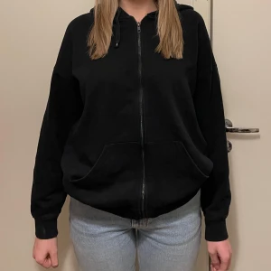 Svart hoodie från Bikbok - Säljer en svart hoodie från Bikbok med dragkedja och huva. Perfekt för en avslappnad stil. Den har långa ärmar och en bekväm passform.