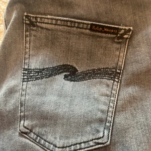 Grå jeans från Nudie Jeans - Snygga grå jeans från Nudie Jeans med klassisk femficksdesign och broderad bakficka. Perfekta för en stilren look med en bekväm passform. Ny pris 1600kr mitt pris 1000 pris kan diskuteras 👍🏻