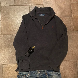 Ralph Lauren Half Zip Large - Snygg mörkgrå Half/Quarter Zip från Polo Ralph Lauren med dragkedja och broderad logga i rött på bröstet. Perfekt för en stilren och avslappnad look. Riktigt gott skick!
