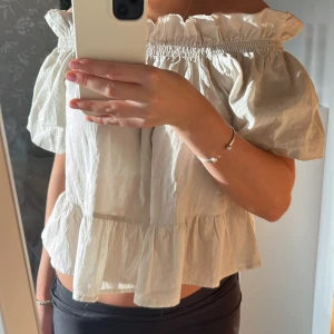 Beige offshoulder blus - Säljer en söt beige offshoulder blus med volangdetaljer. Perfekt för varma sommardagar. Blusen har en luftig passform och korta ärmar.