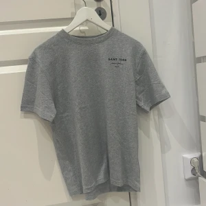 Grå t-shirt från GANT - Säljer en stilren grå t-shirt från GANT med tryck på bröstet. Perfekt för en avslappnad look. Tillverkad i mjukt material för extra komfort.