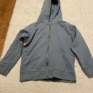 Blå huvtröja med dragkedja - Säljer en bekväm blå huvtröja med dragkedja och fickor framtill. Perfekt för en avslappnad stil. Tröjan har långa ärmar och en praktisk huva.