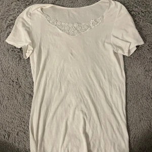Vit t-shirt med spetsdetalj - Säljer en enkel och stilren vit t-shirt med spetsdetalj vid halsringningen. Perfekt för en avslappnad look. Tunn och luftig i materialet, nästan aldrig använd.